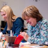 Zwei lachende Frauen arbeiten begeistert an ihrem selbst entworfenen Silberschmuck – ideales Erlebnis für Geburtstagsfeier, Geschenk oder kreatives Teamevent/Teambuilding in Basel